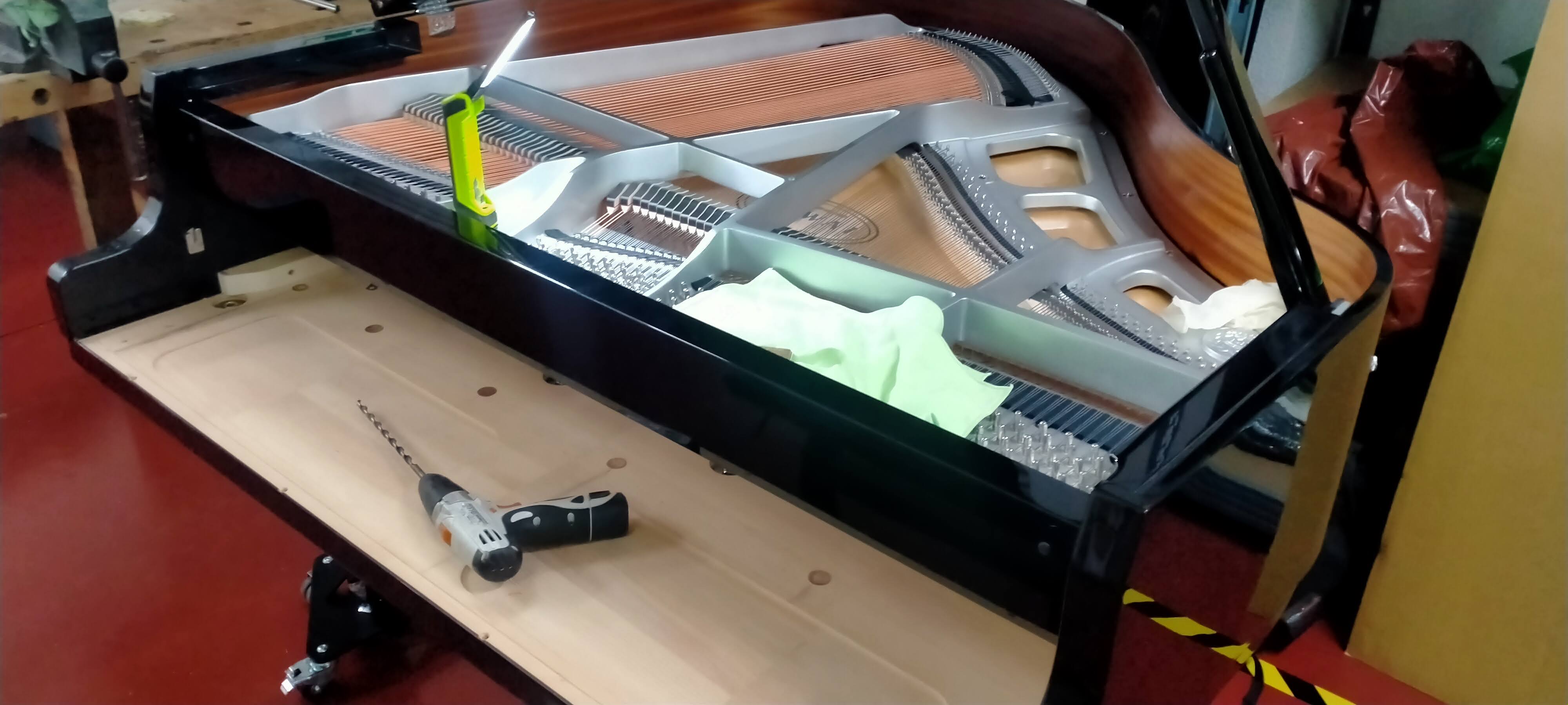 Piano de cola negro en taller con bastidor y cuerdas visibles